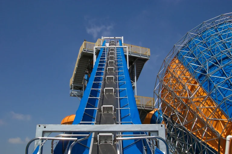 Blue ride conveyor and access stairs at an amusement park under a clear sky