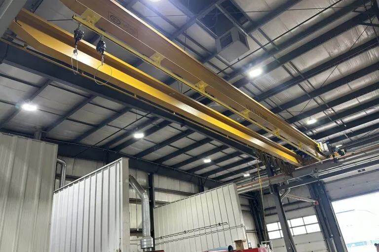 The full 44 ft run of yellow rigid rail beneath the crane bridge, seen from the shop floor.