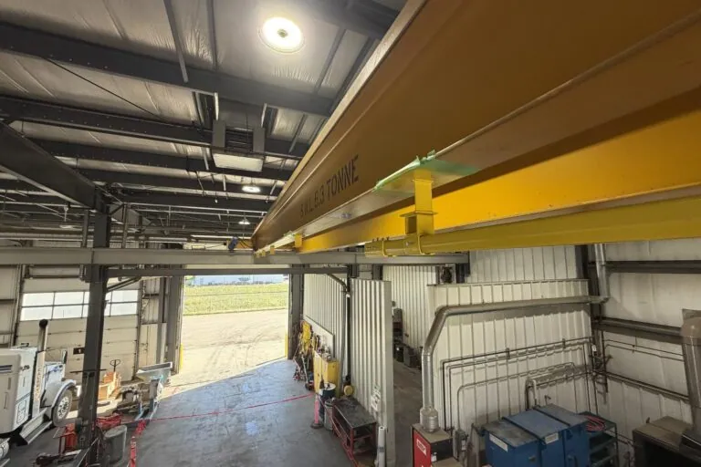 A stand-off drop and hanger carrying the rigid rail below the crane beam, painted safety yellow.