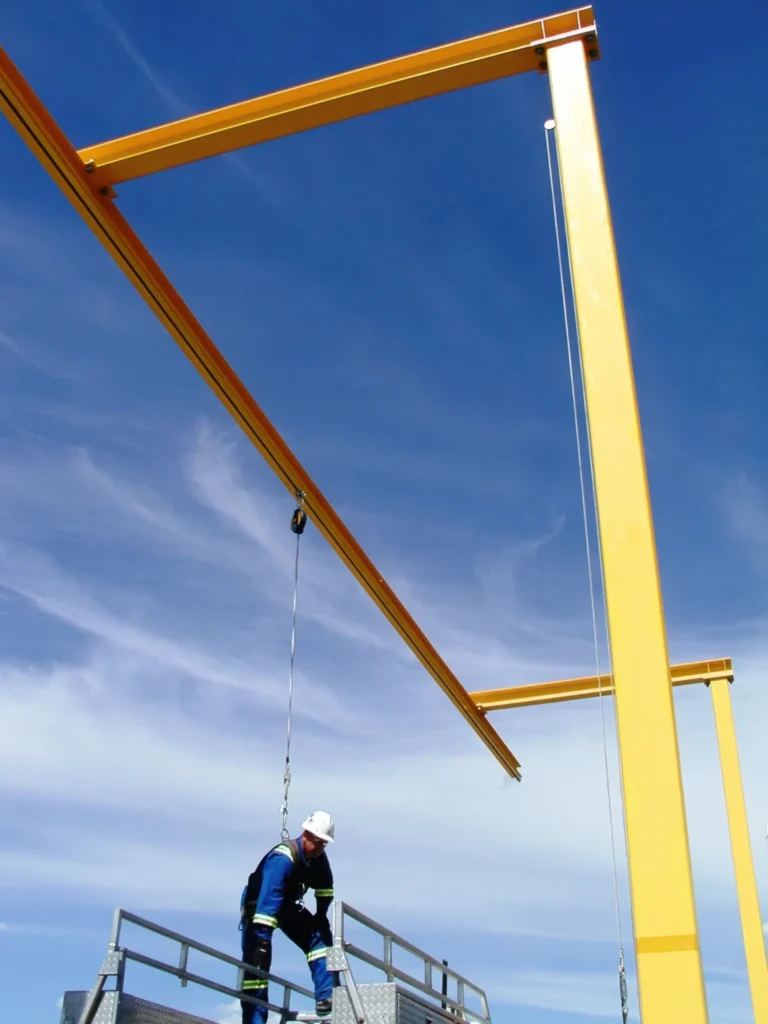 Worker on an elevated platform tied off beneath a yellow freestanding rigid rail frame