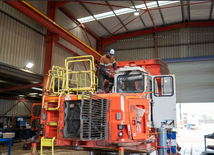 Technician working on top of a mining haul truck cab in a service bay, guardrail on the deck