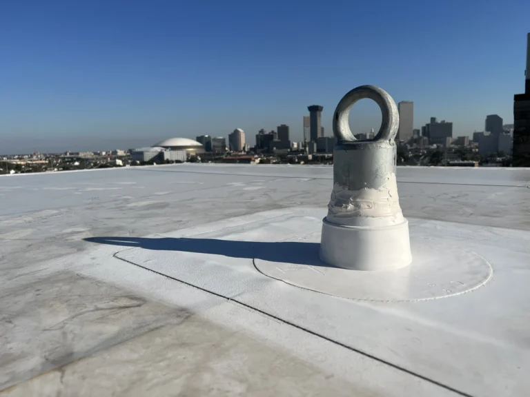 Single-point roof anchor post with a forged eye flashed into a membrane roof with a city skyline behind