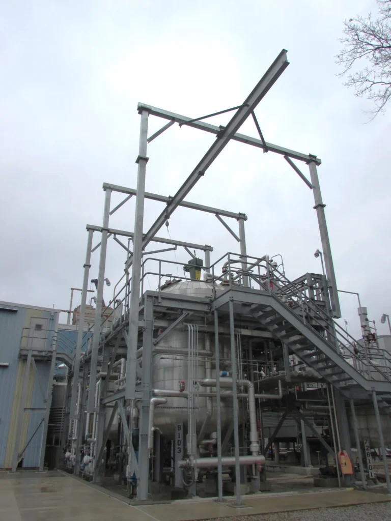 Overhead rigid rail frame above a process structure with stairs and piping