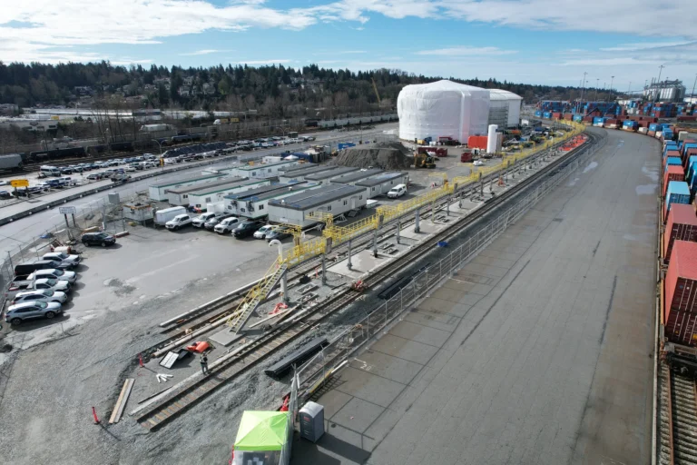 Aerial view of a long access platform with yellow guardrail beside the tracks in an intermodal rail yard