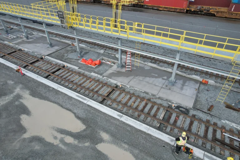 Yellow guardrail and fixed ladders on a rail-side platform with a crew member working at track level