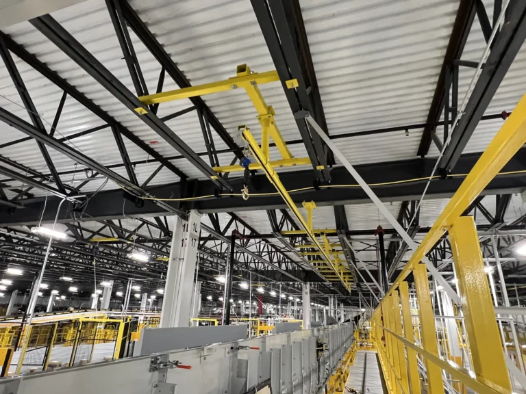 Yellow overhead rigid rail and guardrail along a conveyor catwalk inside a distribution facility