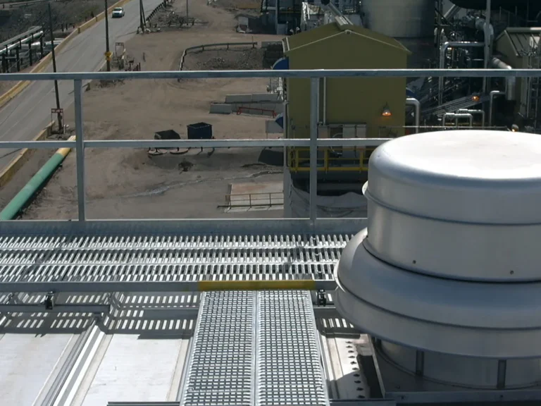 Grated rooftop walkway with guardrail running past a rooftop exhaust fan