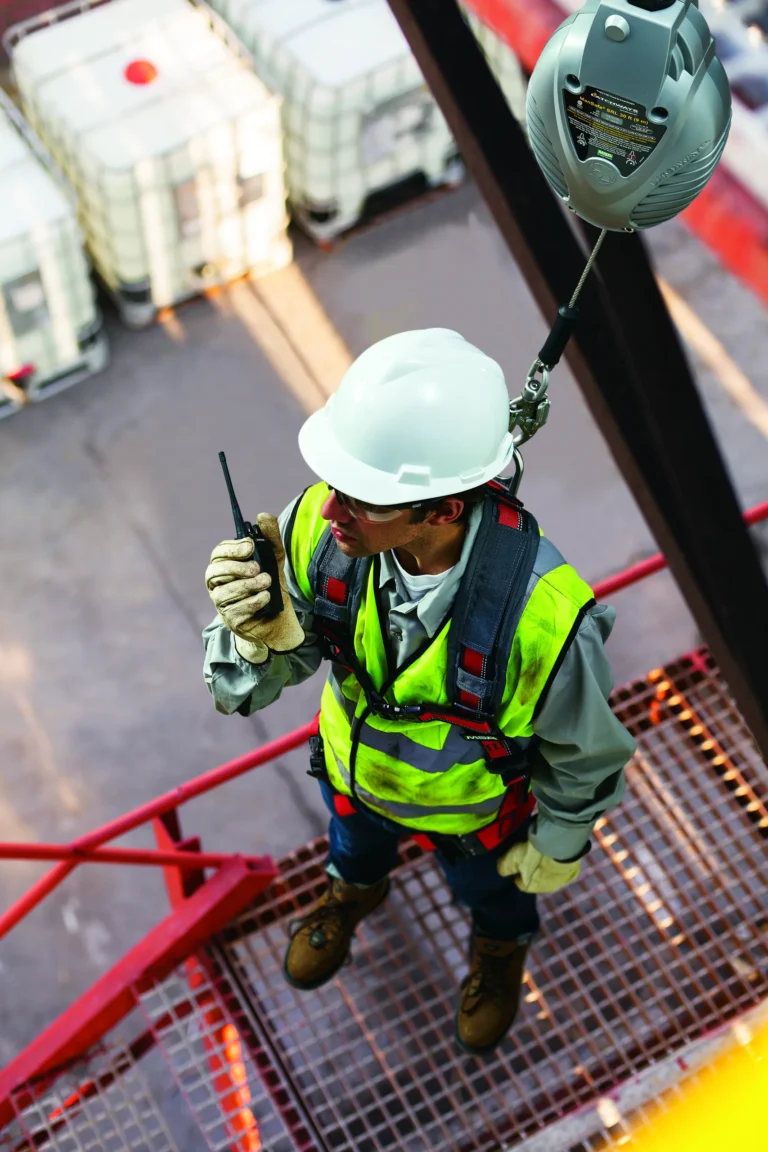 Worker in a hard hat and harness tied off to a self-retracting lifeline on an elevated grated platform